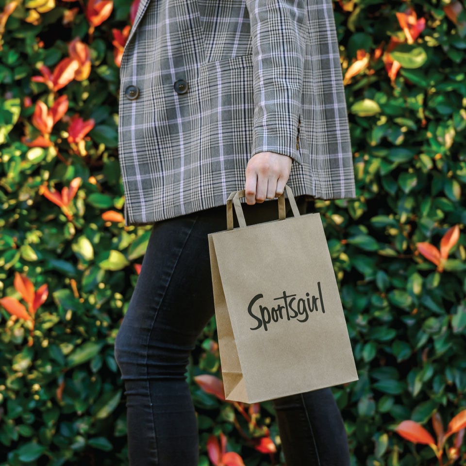 Woman walking with Sportsgirl paper bag. 