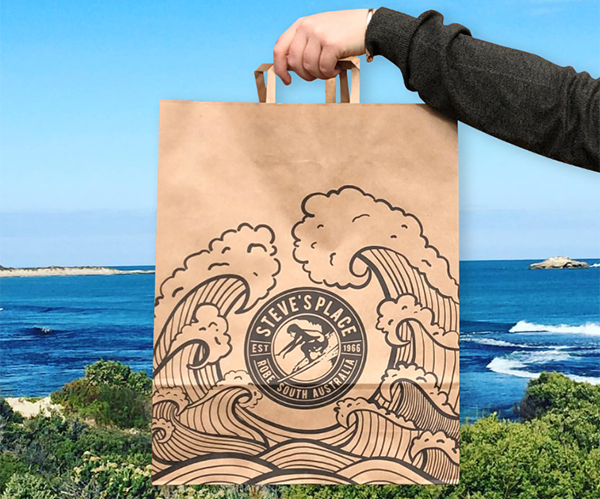 Image of a custom print paper carry bag being held infront of the ocean