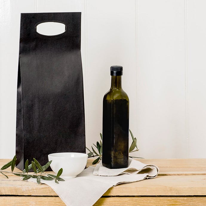 Image of olive oil bottle and herb bowl sitting beside a black paper wine bag. 