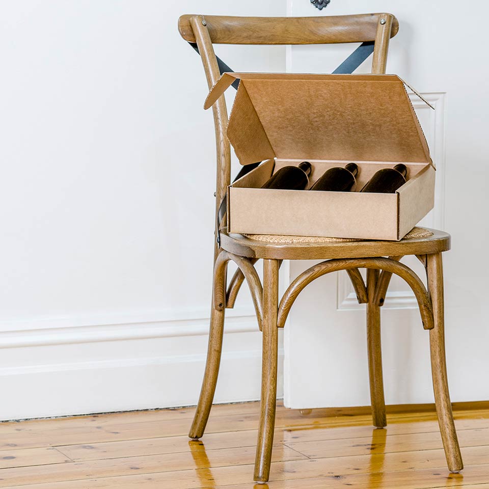 Picture of three wine bottles sitting in a PaperPak shipping carton on a wooden chair